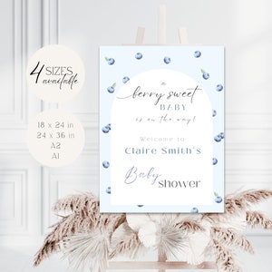 May include: A blue and white baby shower sign with blueberries and the text "A berry sweet baby is on the way!" and "Welcome to Claire Smith's Baby Shower".