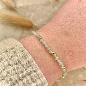 May include: A delicate bracelet featuring small, pale green beads interspersed with gold-colored accents. The bracelet is worn on a wrist, showcasing its subtle elegance. The beads appear to be semi-translucent, adding a touch of sophistication to the jewelry.