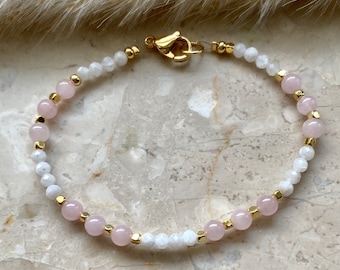 May include: A delicate bracelet with alternating white and pink beads, accented with gold accents. The bracelet features a gold clasp.