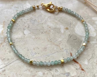May include: A delicate bracelet featuring small, faceted, pale green gemstone beads interspersed with tiny, polished gold-tone metal spacer beads. The bracelet is secured with a gold-tone lobster claw clasp and a small jump ring, creating a refined look.