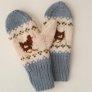 May include: A pair of blue and white knitted mittens with a brown chicken design. The mittens have a white cuff and a blue body with a white and brown pattern.