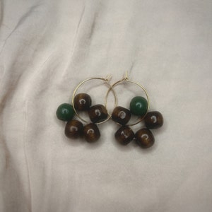 May include: Gold hoop earrings with brown and green wooden beads.