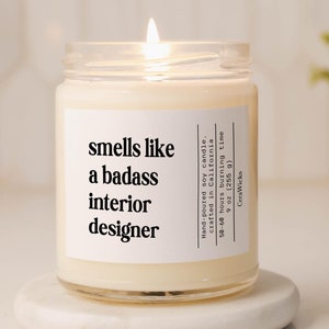May include: A white soy candle with a clear glass jar and a white label that reads "smells like a badass interior designer".