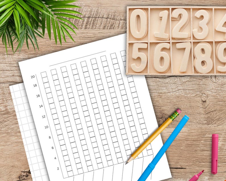 May include: A wooden tray with the numbers 0-9, a grid chart, and a pencil and markers on a wooden surface. The chart has a grid of squares with numbers along the side. The pencil is yellow with a pink eraser. The markers are pink and blue.