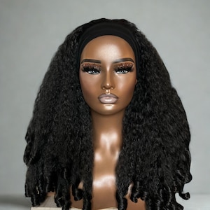 May include: A mannequin head with a dark complexion, wearing a black headband and a long, textured black wig. The wig features voluminous, tightly curled strands. The mannequin has detailed makeup, including prominent eyelashes and defined eyebrows. The background is a solid, neutral gray.