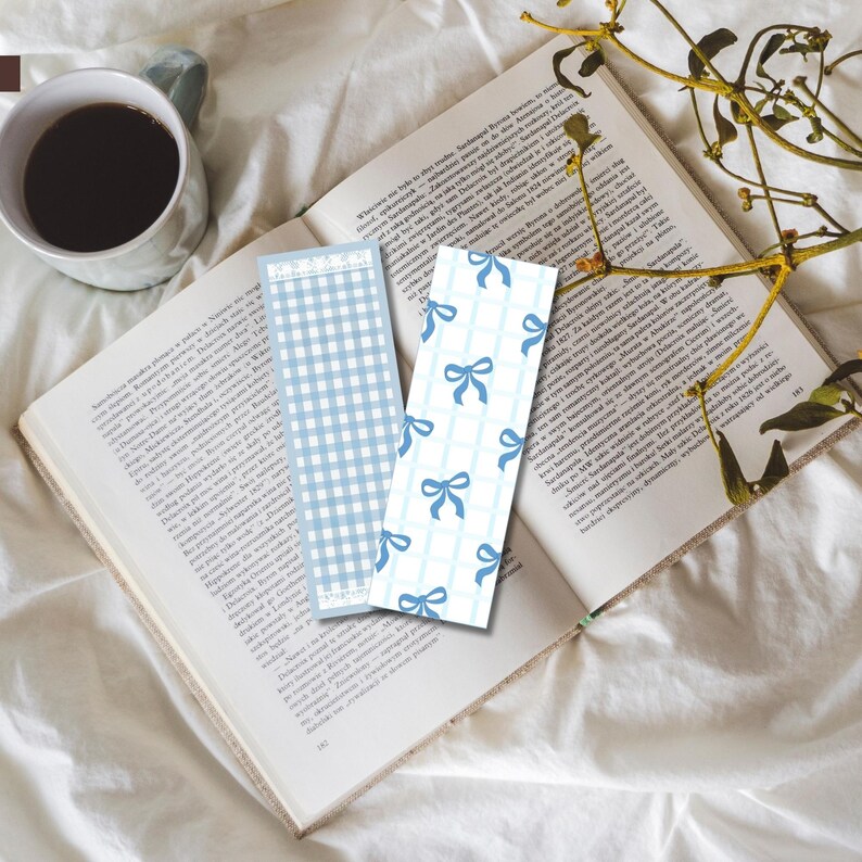 May include: Two blue and white patterned bookmarks. One bookmark has a gingham pattern and the other has a pattern of blue bows on a white background. The bookmarks are on top of a book.