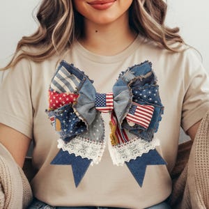 May include: A large denim hair bow with a patchwork design incorporating American flag patterns. The bow includes stars and stripes, and is trimmed with white lace. The bow is a mix of blue, red, and white.