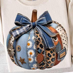 May include: A decorative pumpkin ornament featuring a patchwork design of denim, leopard print, white daisy patterns, and black polka dots. It is topped with a large denim bow and includes metal accents like a star, flower, and a tag reading grateful.