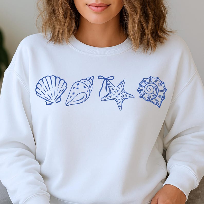 Puede incluir: Sudadera blanca con un dibujo lineal azul de conchas marinas y una estrella de mar. El dise&ntilde;o incluye una concha de vieira, una concha de caracola, una estrella de mar con lazo y una concha en espiral. La sudadera es de estilo casual y c&oacute;modo.