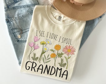 May include: A beige t-shirt with a floral design and the text "I see. I love. I spoil. Grandma".