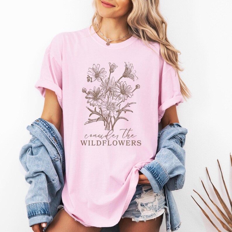 May include: A pink t-shirt with a brown line drawing of a bouquet of wildflowers and the text "consider the wildflowers".