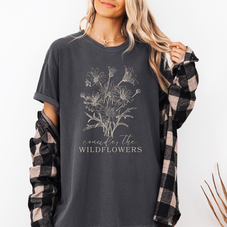 May include: A dark gray t-shirt with a white graphic of wildflowers and the text "consider the wildflowers".