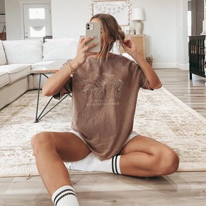 May include: A brown t-shirt with a floral design and the text "Fearfully and Wonderfully Made".