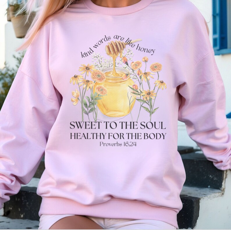 Puede incluir: Sudadera rosa con un gr&aacute;fico de un tarro de miel y flores. El texto dice "Kind words are like honey, Sweet to the soul, Healthy for the body, Proverbs 16:24".