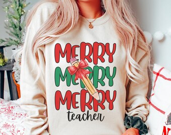 Op de afbeelding: Een crèmekleurige trui met de tekst "Merry Merry Merry teacher" in rood en groen. Een potlood met een rode strik is getekend tussen de woorden "Merry".