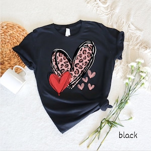 May include: Black t-shirt with a pink and black leopard print heart design and a red heart. The design includes smaller pink hearts.