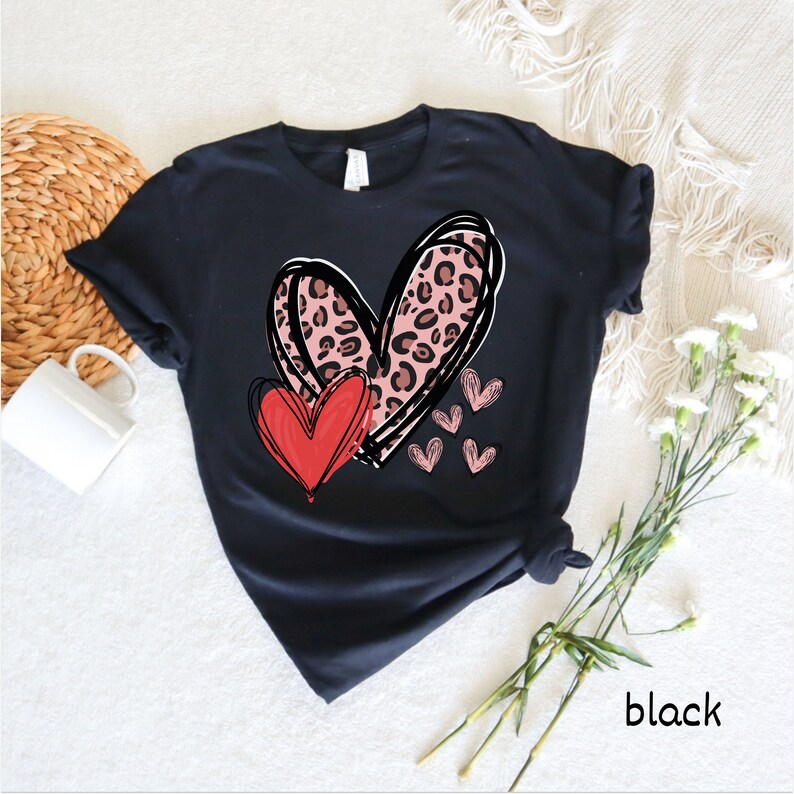 May include: Black t-shirt with a pink and black leopard print heart design and a red heart. The design includes smaller pink hearts.