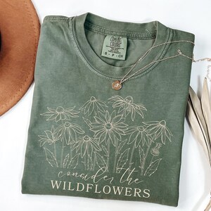 May include: A green t-shirt with a white outline of wildflowers and the text "consider the wildflowers".