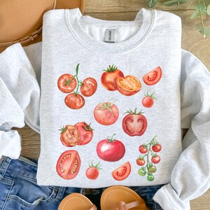 May include: A gray sweatshirt with a watercolor design of red tomatoes. The tomatoes are in various sizes and shapes, some are whole and some are sliced.