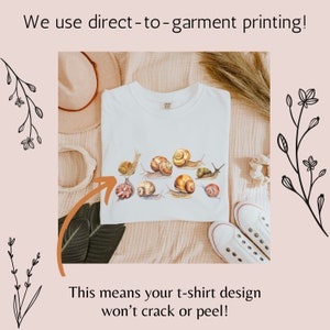 May include: White t-shirt with a design of multiple snails in shades of brown and beige. The text "We use direct-to-garment printing! This means your t-shirt design won't crack or peel!" is visible on the image.