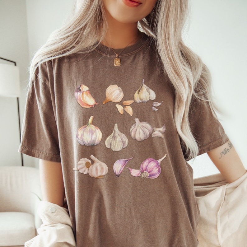 May include: A brown t-shirt with a graphic print of various garlic cloves in different shades of brown, pink, and white.