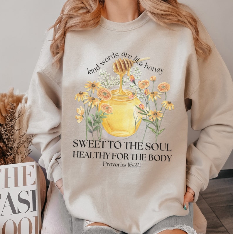 Puede incluir: Sudadera beige con un gr&aacute;fico de un tarro de miel y flores. El texto dice "Kind words are like honey, Sweet to the soul, Healthy for the body, Proverbs 16:24".
