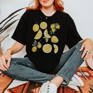 Pu&ograve; includere: Una maglietta nera con una stampa grafica di limoni e fette di limone. I limoni sono gialli e lo sfondo &egrave; nero.