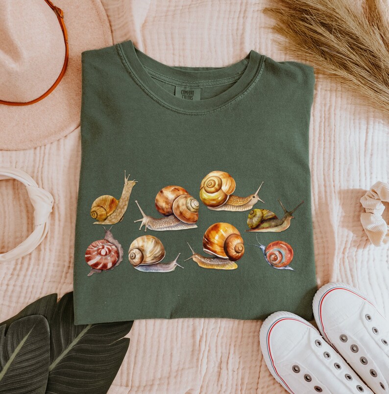 May include: A green t-shirt with a print of multiple snails in various colors and patterns. The snails are arranged in a cluster on the front of the shirt.