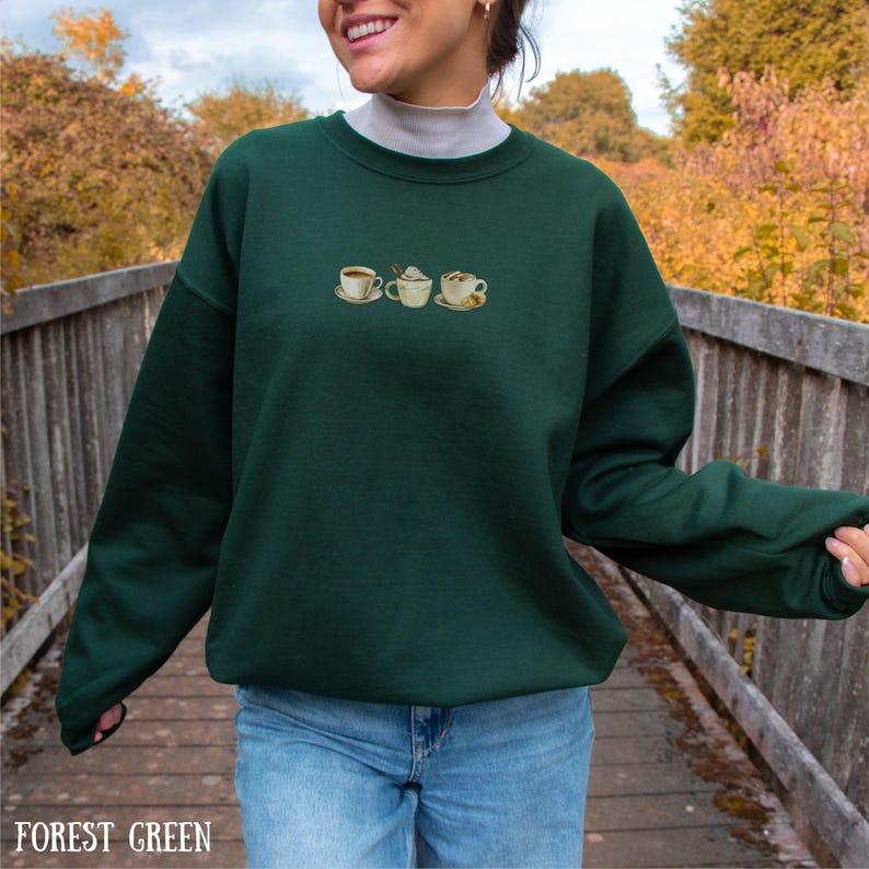 May include: Forest green sweatshirt with embroidered coffee cup designs. The sweatshirt features a crew neck and long sleeves. The text "FOREST GREEN" is displayed at the bottom of the image.