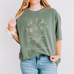 May include: A green t-shirt with a white outline of a bouquet of wildflowers and the text "consider the wildflowers".