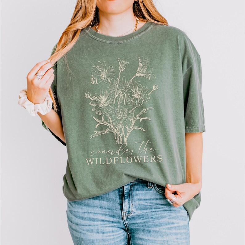 May include: A green t-shirt with a white outline of a bouquet of wildflowers and the text "consider the wildflowers".