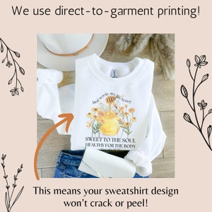 Puede incluir: Sudadera blanca con un dise&ntilde;o de tarro de miel y flores. El texto en la sudadera dice "Kind words are like honey, Sweet to the soul, Healthy for the body".