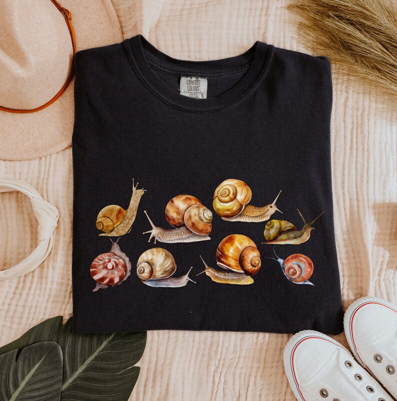 May include: Black t-shirt with a graphic print of multiple snails in various colors and patterns. The text "Comfort Colors" is visible on the tag.
