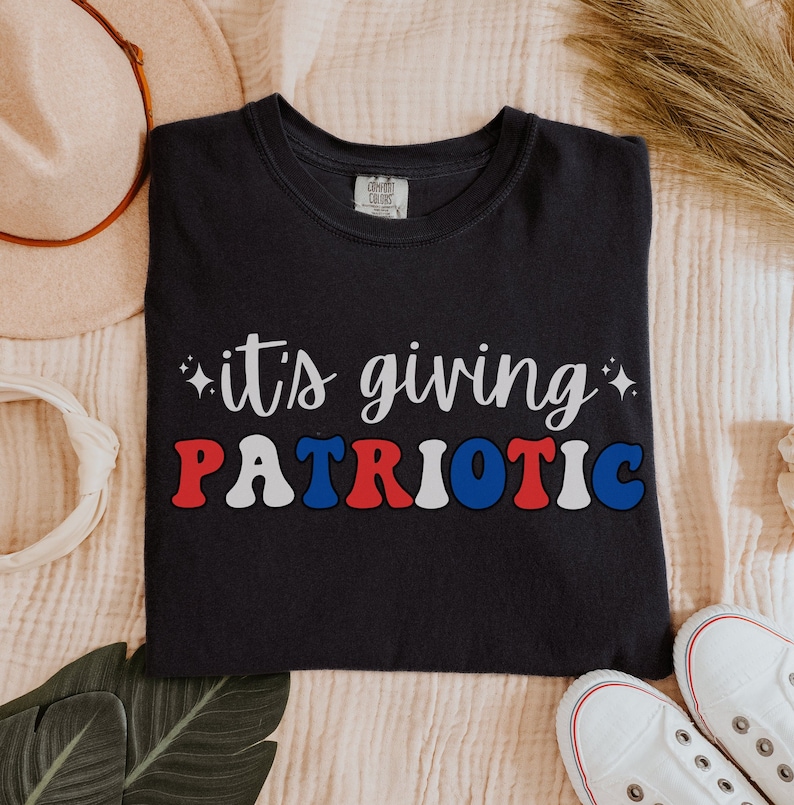 Pu&ograve; includere: T-shirt blu navy con la scritta "it's giving PATRIOTIC" in bianco, rosso e blu. La maglietta ha un girocollo e maniche corte. Il design &egrave; centrato sul davanti.
