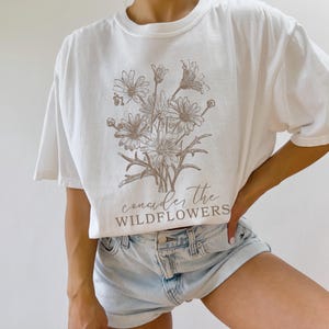 May include: White t-shirt with a brown floral design and the text "consider the wildflowers" printed on the front.