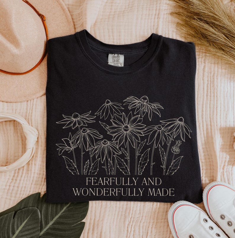 May include: A black t-shirt with a white outline of flowers and the text "Fearfully and Wonderfully Made".