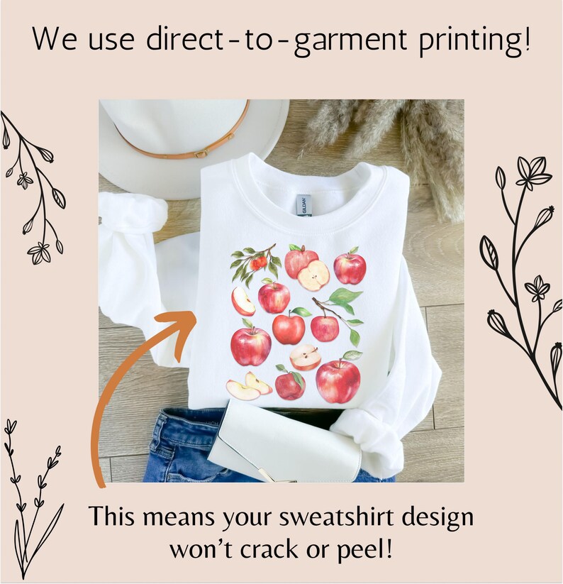 Pu&ograve; includere: Felpa bianca con un design di mele rosse. Il testo "We use direct-to-garment printing!" &egrave; nella parte superiore dell'immagine. Il testo "This means your sweatshirt design won't crack or peel!" &egrave; nella parte inferiore dell'immagine.