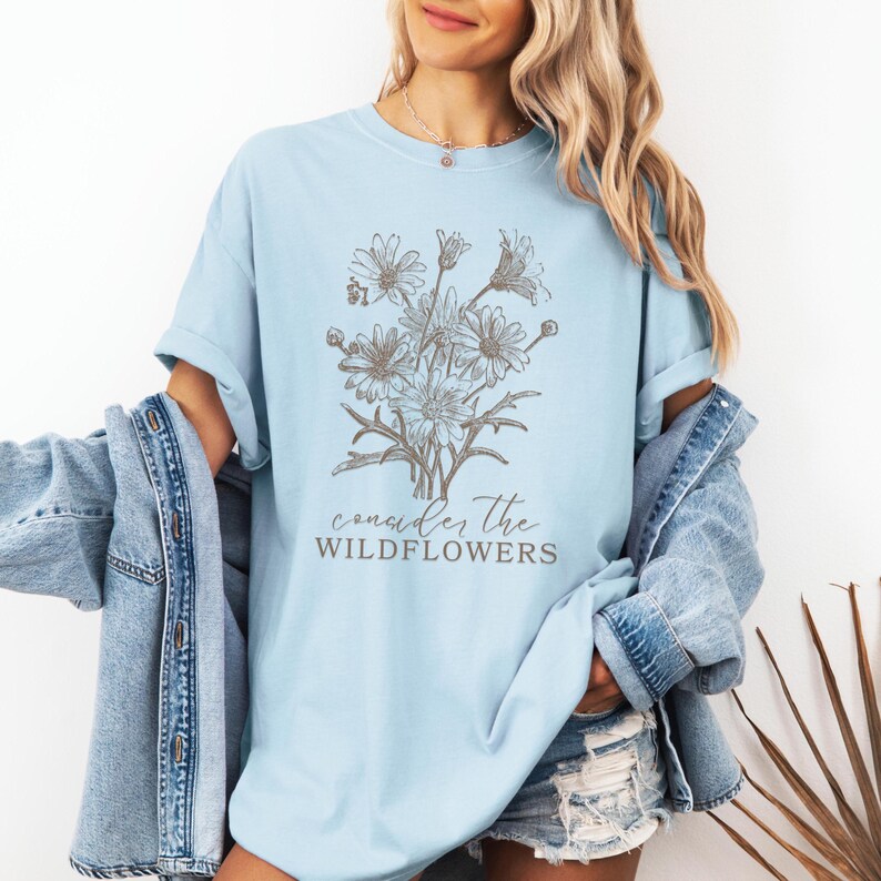 May include: A light blue t-shirt with a graphic of a bouquet of wildflowers and the text "consider the wildflowers".