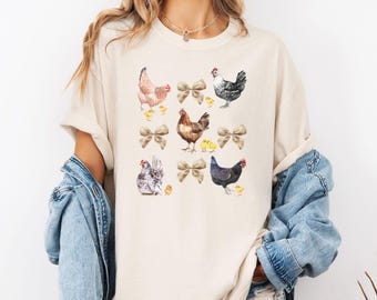 May include: A beige t-shirt with a repeating pattern of brown, black, and grey chickens and chicks with brown bows.