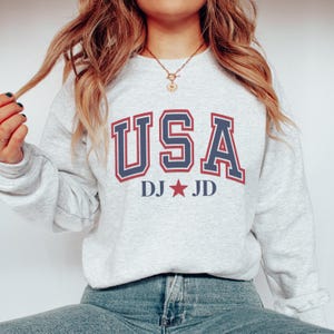 May include: A gray sweatshirt with a navy blue and red "USA" graphic with a red star and the text "DJ JD" underneath.