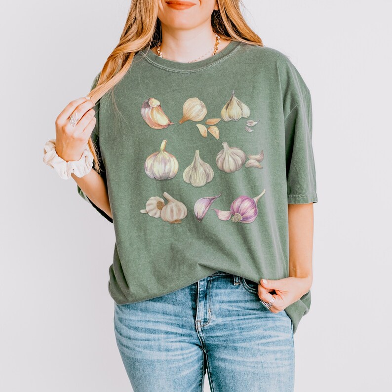 May include: A green t-shirt with a graphic print of various garlic cloves in different shades of brown, white, and purple.
