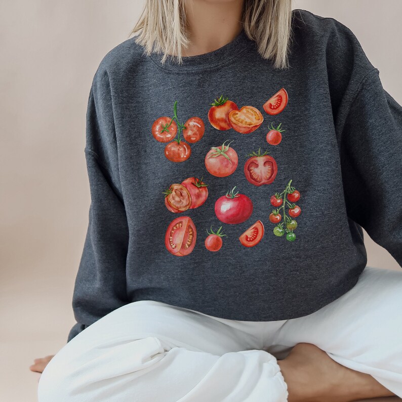 May include: A dark gray sweatshirt with a watercolor print of red tomatoes. The tomatoes are arranged in a variety of ways, including whole, sliced, and in clusters.