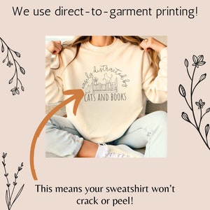 May include: A cream colored sweatshirt with the text "easily distracted by cats and books" in black. The text is in a semi-circle with a graphic of cats and books inside the circle.