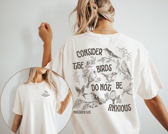 May include: Cream-coloured t-shirt featuring a bird graphic and the text "Consider the birds, do not be anxious" and "Matthew 6:26". The shirt has a loose fit.