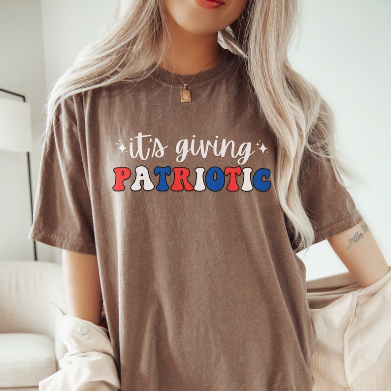 Pu&ograve; includere: T-shirt marrone con la scritta "it's giving PATRIOTIC" in lettere rosse, bianche e blu. Il testo ha uno stile retr&ograve;. La t-shirt &egrave; un capo casual, adatto all'uso quotidiano.