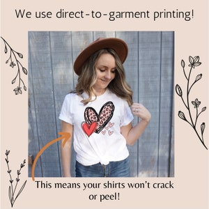 May include: A white t-shirt with a pink and red heart design printed on the front. The text "We use direct-to-garment printing!" is at the top of the image. The text "This means your shirts won't crack or peel!" is at the bottom of the image.