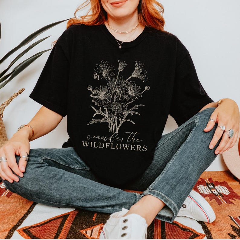 May include: Black t-shirt with a white graphic of wildflowers and the text "consider the wildflowers".