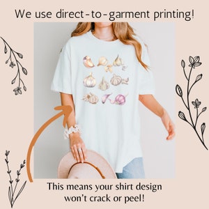 May include: White t-shirt with a watercolor design of garlic cloves. The text "We use direct-to-garment printing! This means your shirt design won't crack or peel!" is printed on the bottom of the image.
