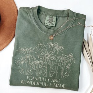 May include: A green t-shirt with a white outline of flowers and the text "Fearfully and Wonderfully Made".