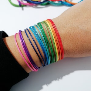 May include: A rainbow colored string bracelet with multiple strands of different colors, including red, orange, yellow, green, blue, indigo, and violet.